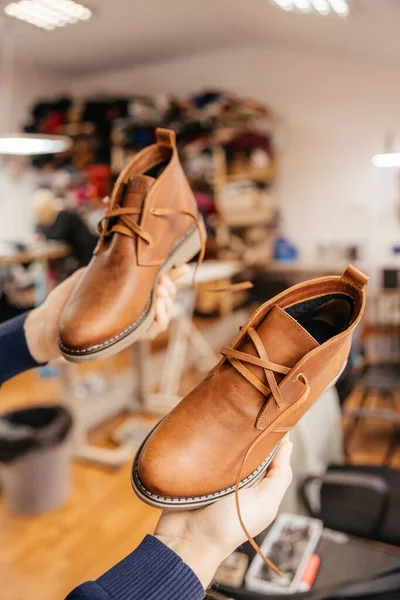 Photo of a pair of quality men\'s leather shoes. Man in apron checking quality of leather details. Manufacturing industry and footwear production concept