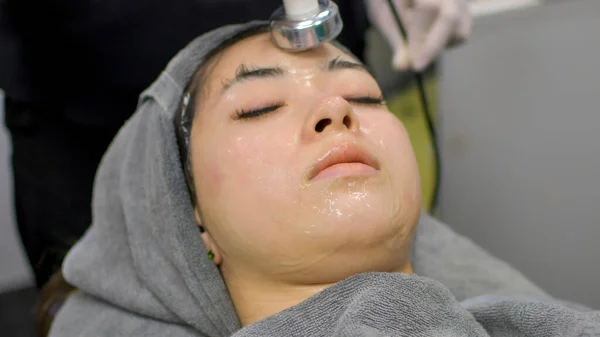 A beautiful Asian woman undergoes facial rejuvenation in a beauty clinic using modern medical equipment. By certified beauty experts according to standards.