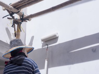 Bir ressam gri beton bir çatının saçaklarının altını boyuyor..