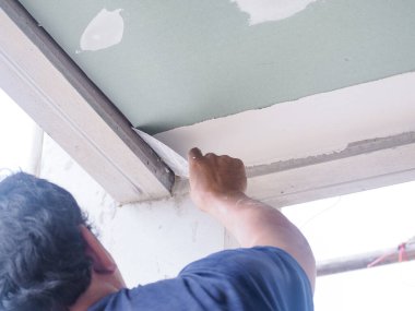 Tavan işçisi, eklemleri bir arada tutmak için tavan eklemlerini yüksek kaliteli beyaz alçıtaşı alçısıyla kaplıyor..