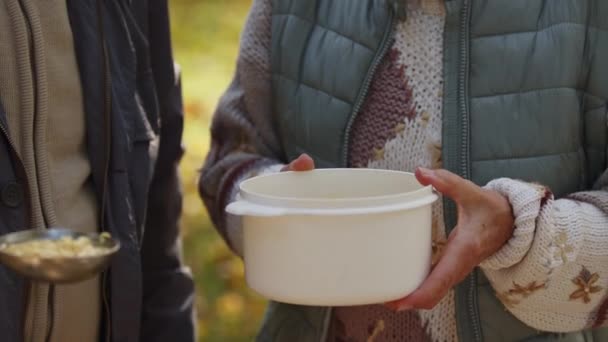Благотворительное мероприятие. Пожилая женщина получает горячую еду. Закрыть на пластиковый контейнер — стоковое видео