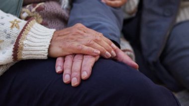 Dışarıda otururken el ele tutuşan yaşlı bir çift. Doğal ışığı kapat