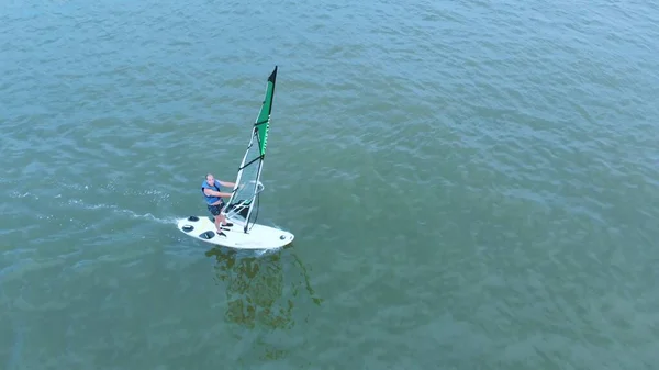 Un homme avec une planche à voile navigue en ligne droite et profite de l'eau équipée pour ce sport — Photo