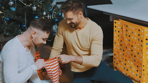 Νεαρό αντρικό ζευγάρι να δίνει δώρα ο ένας στον άλλο με χριστουγεννιάτικες κάλτσες. Ομοφυλοφιλική σχέση και χειμερινές διακοπές έννοια — Φωτογραφία Αρχείου