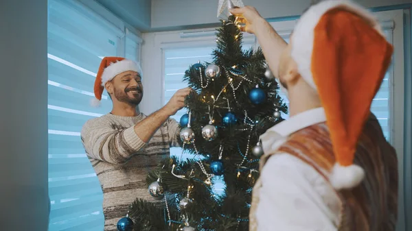Χριστουγεννιάτικη διακόσμηση. Γκέι ζευγάρι που διασκεδάζει διακοσμώντας χριστουγεννιάτικο δέντρο — Φωτογραφία Αρχείου