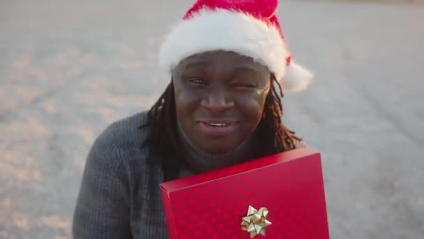 Glad svart man med tomte hatt håller röd insvept julklapp. Hög vinkel skott — Stockvideo