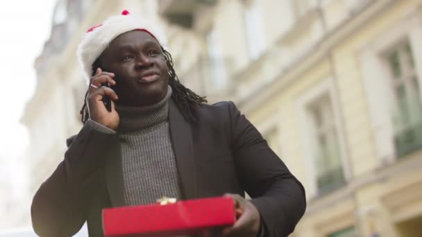 黑衣人头戴圣诞帽，头戴红色礼品盒，街上有电话 — 图库视频影像