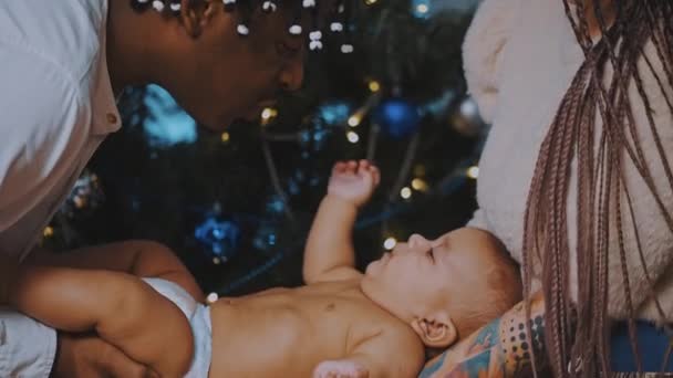 Pais afro-americanos segurando bebê recém-nascido na frente da árvore de Natal — Vídeo de Stock