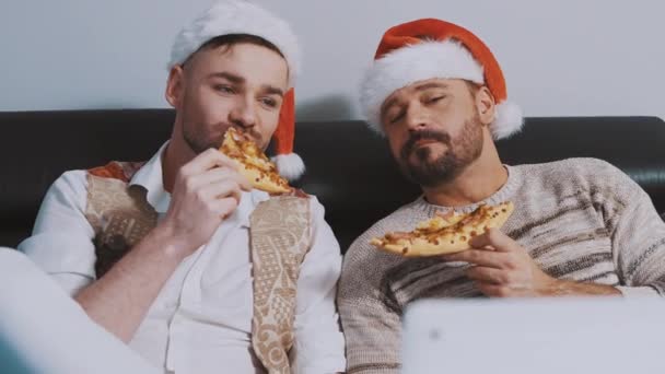 Lovely gay male couple with christmas hats eating pizza and watching movies on the christmas eve — Stock Video