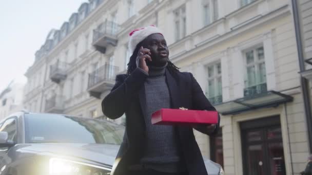 Afrykański Amerykanin w kapeluszu i prezencie, rozmawiający przez telefon przed samochodem. — Wideo stockowe