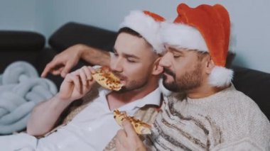 Noel şapkalı, pizza yiyen ve Noel arifesinde film izleyen sevimli eşcinsel çift.