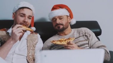 Noel şapkalı, pizza yiyen ve Noel arifesinde film izleyen sevimli eşcinsel çift.