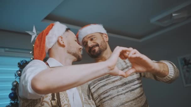Счастливая гей-пара празднует Рождество. Создание формы сердца с помощью рук — стоковое видео