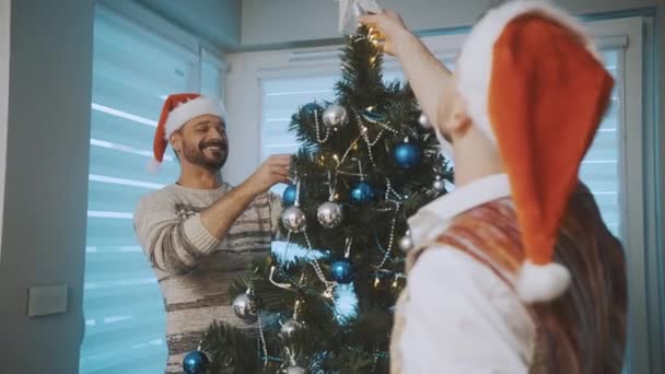 Christmas tree decoration. Gay male couple having fun decorating christmas tree — Stock Video