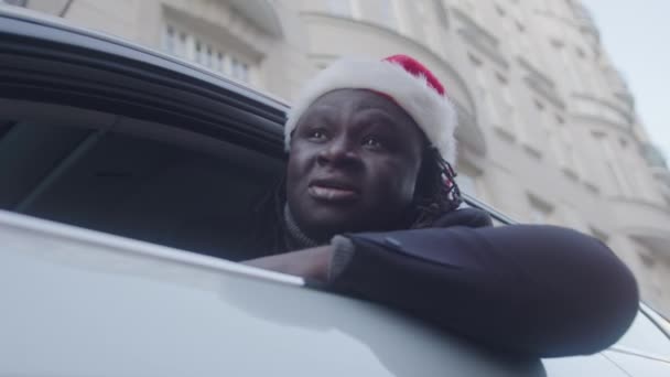 Homme d'affaires afro-américain avec chapeau de Père Noël regardant par la fenêtre de sa voiture — Video