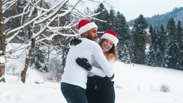 Szczęśliwa młoda para bawiąca się na śniegu w świątecznych kapeluszach. Przytulanie i śmiech. Koncepcja ducha Bożego Narodzenia — Wideo stockowe