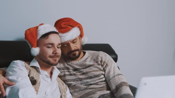 Jovem gay casal com santa chapéus abraçando e assistindo filmes no Natal véspera — Vídeo de Stock