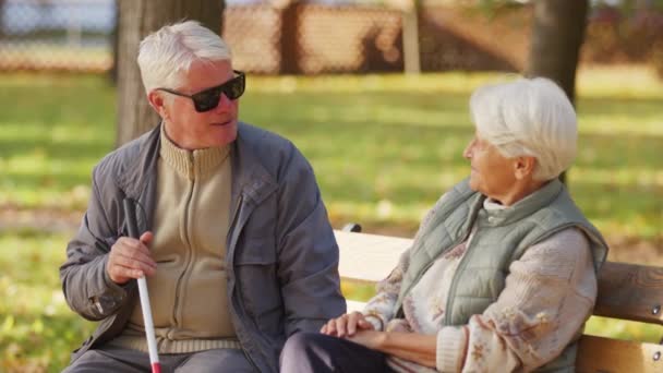 Blinder älterer Mann sitzt mit Frau auf Bank im Park und hält Blindenstock — Stockvideo