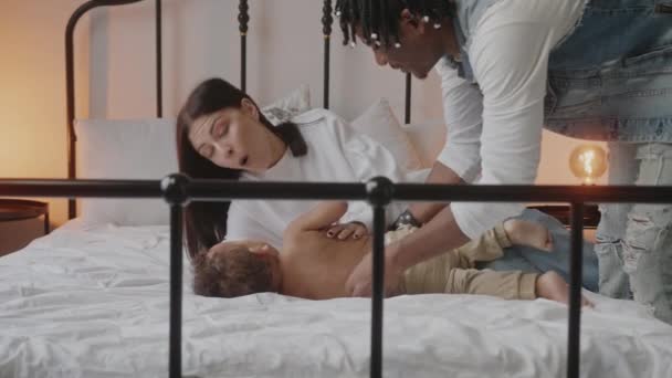 Happy mixed race family playing with baby on the bed. Father tickling his son — Stockvideo