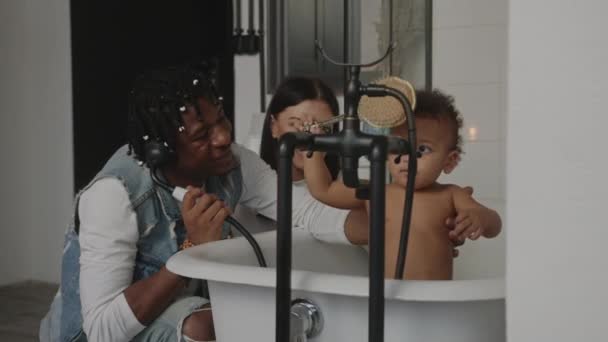 Bagnetto. razza mista bambino giocare in un bagno con pennello mentre caucasico madre e afro-americano padre stanno guardando — Video Stock