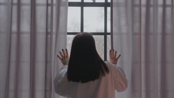 Ung kvinna öppnar gardinen tittar genom fönstret. Glad självsäker dam njuter av vacker utsikt och drömmer hemma — Stockvideo