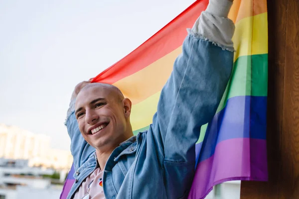 Feliz persona queer no binaria orgullosamente sosteniendo la bandera del orgullo del arco iris y sonriendo. Primer plano mediano. — Foto de Stock