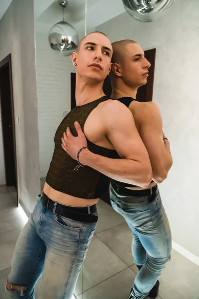 Europeu queer lgbt pessoa em preto top tanque e jeans posando dentro de casa ao lado do espelho — Fotografia de Stock