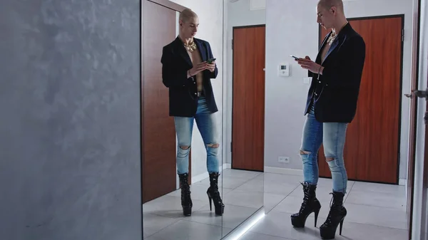 caucasian drag queen preparing themselves for the upcoming show standing in front of the mirror in extremely high heels and taking selfies with a smartphone