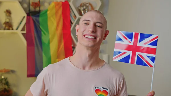 Indoor retrato de um caucasiano orgulhoso sorrindo gay homem acenando bandeira do Reino Unido em seu apartamento. — Fotografia de Stock