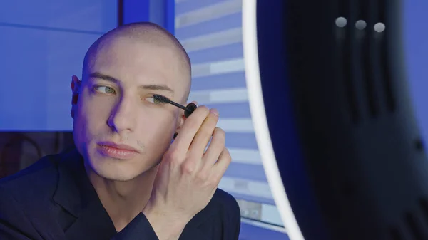 Icke-binär queer person förbereder sig för att gå ut och sätter mascara på ögonfransarna medan du tittar i spegeln — Stockfoto