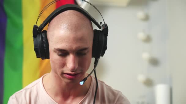一个秃头的同性恋游戏玩家在使用专业耳机玩电子游戏时的近照。背景上的彩虹旗. — 图库视频影像