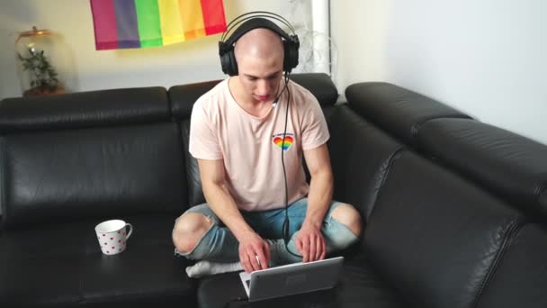 Pemain game aneh Eropa bermain di laptopnya sambil duduk di sofa dan menggunakan headphone profesional. — Stok Video
