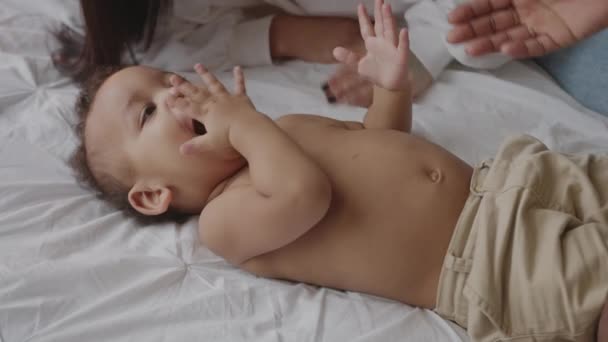 Niedliches Mischlingsbaby legt sich auf Bett und spielt mit seinen Eltern. — Stockvideo