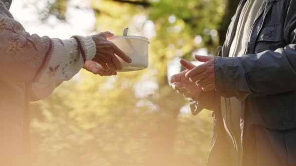 Begreppet att dela mat med människor i nöd. Utomhus bild av två personer som hanterar över en vit plastskål fylld med näringsrik varm soppa. — Stockvideo