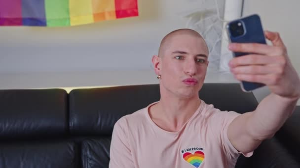 Європейський лисий гей, який розмовляє зі своїм смартфоном, сидить на дивані.. — стокове відео