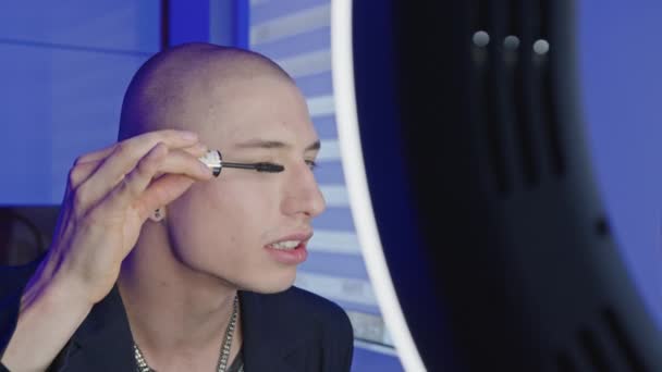 Mladý evropský gay muž dává na make-up a černé řasenky tím, že se podívá do zrcadla a pomocí profesionální lampy v koupelně — Stock video