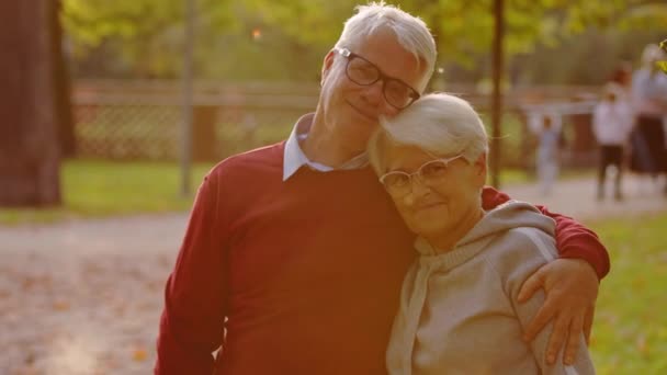 Портрет двух старших бабушек и дедушек, обнимающих и улыбающихся в камеру. Средний крупный план на открытом воздухе. — стоковое видео