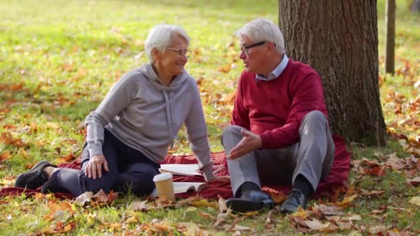 公園の秋のピクニック。草の上に座って話をする2人の年配の年金受給者. — ストック動画