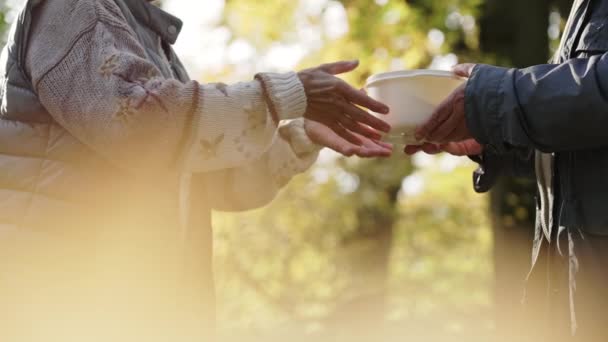 Uma pobre pessoa idosa em situação de rua está a receber uma tigela de refeição quente por um voluntário caucasiano. Tiro exterior. — Vídeo de Stock