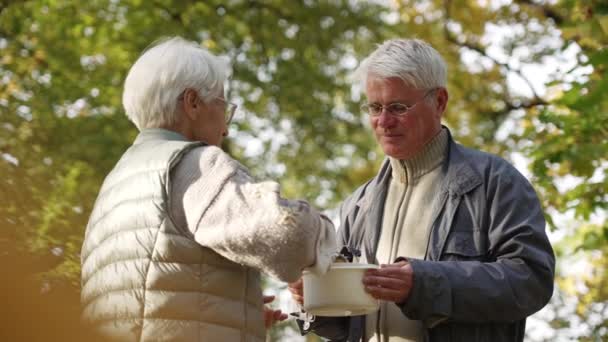 Caucasiano idoso aposentado mulher compartilha sua sopa caseira com desempregado e sem-teto idoso em necessidade. — Vídeo de Stock