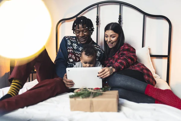 Multiraciale familie Kerstvakantie Concept. Koelen op bed, kijken naar video 's op tablet met weinig gemengde ras baby jongen. — Stockfoto
