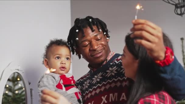 Famiglia multirazziale con adorabile bambino che celebra il Natale tenendo scintille. — Video Stock