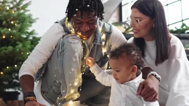 Όμορφη σύγχρονη οικογένεια γιορτάζει την παραμονή των Χριστουγέννων, παίζοντας με τα φώτα των Χριστουγέννων. — Αρχείο Βίντεο