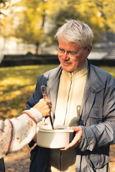 Beyaz, evsiz, yaşlı bir adamla çorba içiyorum. Dikey açık hava çekimi.