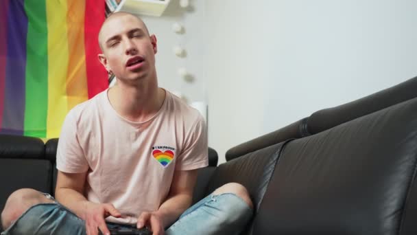Caucásico gay chico perder un juego, romper, y estar enojado consigo mismo. Bandera del arco iris en el fondo. — Vídeo de stock