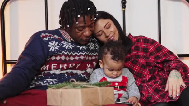 พ่อแม่หลายเชื้อชาติฉลองวันคริสต์มาสอีฟ และนั่งอยู่กับเด็กเล็กบนเตียง . — วีดีโอสต็อก