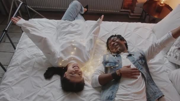 Couple mixte allongé sur leur lit king size, riant et profitant de leur temps libre. — Video