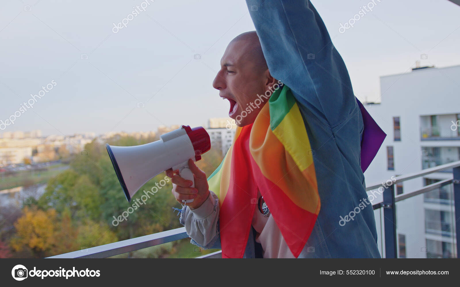 Caucasian proud bisexual man fighting for equality and same sex marriage, wrapped in rainbow flag screams aside in megaphone from his balcony Stock Photo by ©CameraCraft 552320100 photo