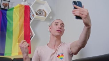 Arka planda akıllı telefon ve gururlu gökkuşağı bayrağıyla takipçileriyle konuşan ibne eylemci..