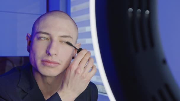 Branco careca gay influenciador criação novo maquiagem tutorial usando rímel para seus seguidores, falando, e sorrindo — Vídeo de Stock